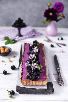 a table topped with a purple tart covered in blackberries and other food items