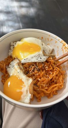 a person holding a bowl of noodles with eggs on top