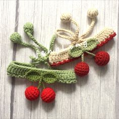 two crocheted cherries hanging from a tree branch with leaves and berries attached to them