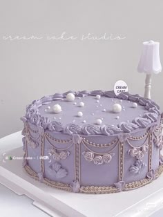 a purple cake sitting on top of a white table next to a lamp and paper