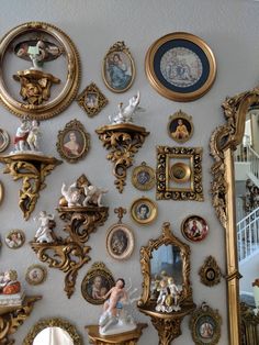 a wall covered in lots of different types of framed pictures and figurines next to a mirror