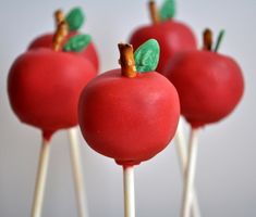 four red apples with green leaves on them sitting on top of toothpick sticks