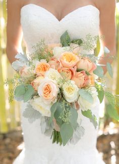 a bride holding a bouquet of peach and white flowers on her wedding day in the woods