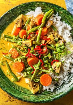 a green bowl filled with rice and veggies on top of a yellow table