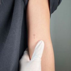 a person with a small cross tattoo on their left arm and the other arm is covered in white gloves