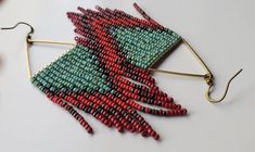 a pair of red and green beaded earrings on a white table next to some beads