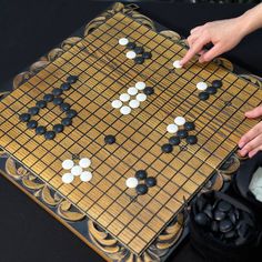 a person is playing a board game with white and black pieces on it, while another hand points at them