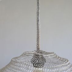 a glass light hanging from the ceiling in front of a white wall with a chain attached to it