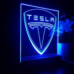 a blue neon sign with the word tesla on it next to a potted plant