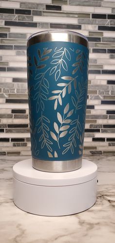 a blue and silver vase sitting on top of a white stand in front of a tile wall