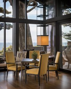 a dining room table with yellow chairs and a lamp in front of large windows overlooking the ocean