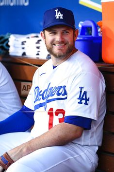 a smiling dodgers baseball player sits in the dugout