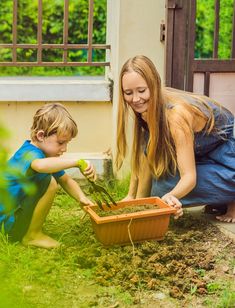 a woman kneeling down next to a little boy who is digging in the dirt with a shovel