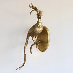 a golden bird is mounted on the wall next to a light fixture with a candle in it's mouth