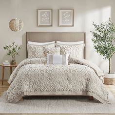 a bed with white comforter and pillows in a room next to a potted plant