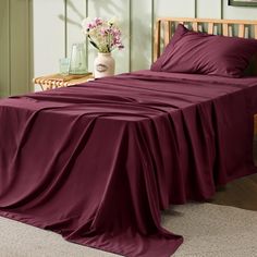 a bed covered in a maroon sheet and pillow cases with flowers on the nightstand next to it