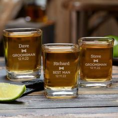 three shot glasses sitting on top of a wooden table next to a slice of lime