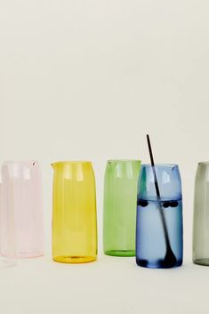 four different colored glass vases with a straw sticking out of the top and bottom