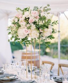 a tall vase filled with pink and white flowers on top of a table covered in silverware