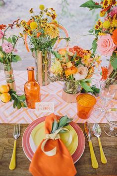 the table is set with orange and yellow flowers in vases, plates, utensils and napkins