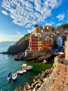 boats are docked in the water next to some buildings on the cliff above the ocean