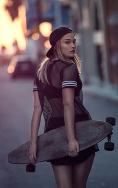 a woman walking down the street with a skateboard in her hand and wearing a hat