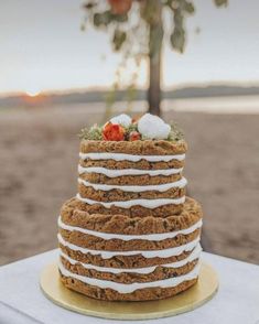 a wedding cake sitting on top of a table next to a tree in the sand