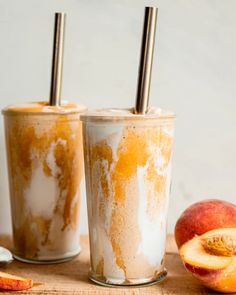 two glasses filled with ice cream and peaches next to an apple on a cutting board