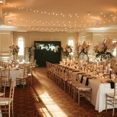 a banquet hall with tables and chairs set up for a formal function, decorated with white flowers and greenery