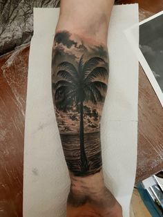 a man's arm with a palm tree and ocean scene tattoo on the forearm