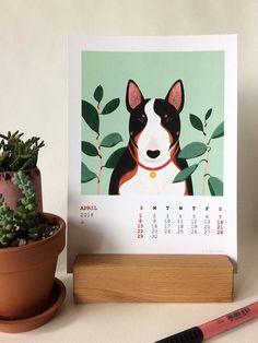 a desk calendar with a dog on it next to a potted plant and pencil