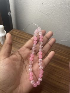 a hand holding some pink beads on a table