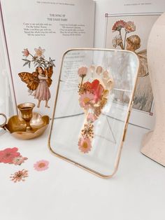 an open book on a table with flowers and fairy figurines next to it