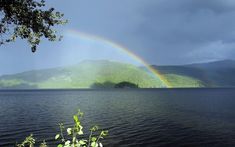 a rainbow shines in the sky over a body of water with mountains in the background