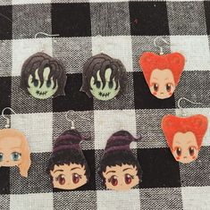 four different anime character earrings on a checkered tablecloth with black and white fabric