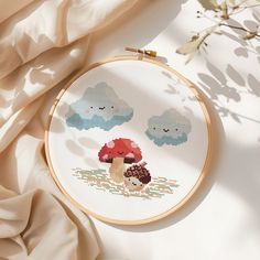 a cross - stitch pattern with mushrooms and clouds on it, next to a plant