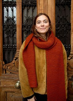 a woman standing in front of a wooden door wearing a red scarf and brown jacket