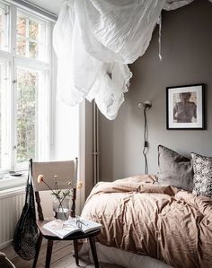 a bed sitting under a window next to a table with a lamp on top of it