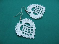 two white crocheted doily earrings on a green surface