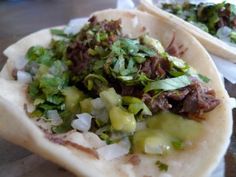 two tacos filled with meat and vegetables on top of a table next to each other