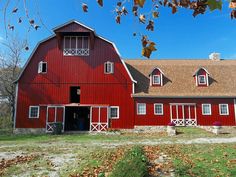 a large red barn with white windows and doors on the front, surrounded by grass and trees