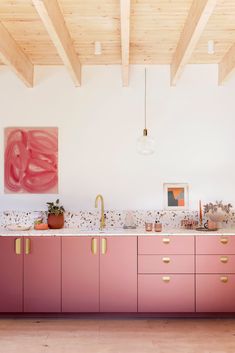 a kitchen with pink cabinets and gold pulls on the doors, along with artwork hanging from the ceiling