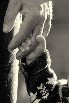 a black and white photo of a person holding the hand of a child's hand