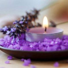 a candle that is on some kind of plate filled with purple flowers and lavender petals