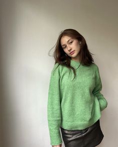 a woman in a green sweater and black leather skirt poses for the camera with her hand on her hip