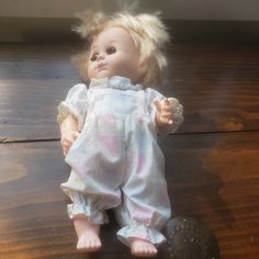 a doll with blonde hair sitting on top of a wooden floor next to a black object