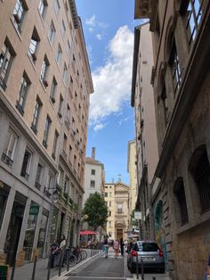 people are walking down the street in an old european city with tall buildings on either side