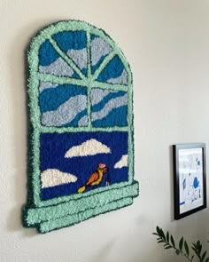 a wall hanging on the side of a white wall with a blue and green window