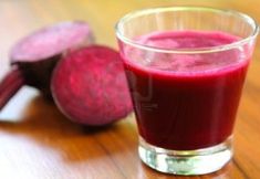 a glass filled with beet juice next to sliced beets on a wooden table