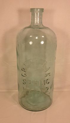 an old glass bottle is sitting on a white tableclothed surface, with the word spring written in cursive writing